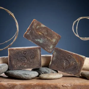 Savon café curcuma exfoliant artisanal Savonnerie des Monédières posés sur galets et bois flotté, texture brun foncé grainé saponifié à froid Corrèze