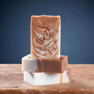 Trois pains de savon cannelle avocat Savonnerie des Monédières empilés sur bois, marbrage bicolore brun-blanc avec motif gravé, texture très dure surgras 6%