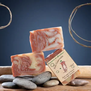 Savon ricin karité Bulle Essentielle artisanal Corrèze posés sur galets, marbrage rose et crème, étiquette Savonnerie des Monédières saponifié à froid