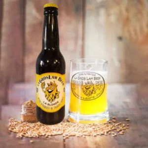 Une bouteille de bière blonde artisanal 33 cl de la Brasserie de la Quiotte sur une table en bois, avec des ingrédients comme des malts et des houblons.