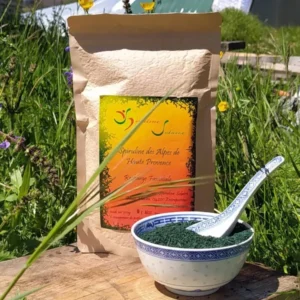 Sachet kraft 300g de spiruline en paillettes croustillantes Spiruline Solaire posé en pleine nature à Entrepierres, avec un bol bleu et blanc rempli de paillettes vertes et une cuillère en porcelaine, Alpes de Haute Provence