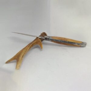 Couteau Laguiole artisanal de 12 cm avec manche en bois d'olivier ouvert, posé sur une surface claire. La lame fine et tranchante en acier inoxydable se détache nettement sur le fond neutre. La poignée en bois d'olivier arbore des nuances de couleur naturelles et un grain distinct. Les éléments métalliques, comme la mitre et le ressort guilloché avec l'abeille en relief, ajoutent une touche d'élégance au couteau, qui reflète un savoir-faire traditionnel.