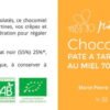 L'image montre l'étiquette de design plat d'un pot de pâte à tartiner "Chocomiel" de la marque "Miellerie du Baume". La moitié gauche de l'étiquette est de couleur crème et contient un texte descriptif qui dit : "Pour une pause gourmande bien méritée. Avec sa texture onctueuse et ses arômes chocolatés, ce chocomiel est le produit idéal pour accompagner vos tartines, vos crêpes et autres gaufres. Il est à consommer sans modération pour régaler petits et grands." La composition est listée comme "miel fleurs d'été 70%, chocolat noir (55%) 25%, noisettes torréfiées poudre 5%*" avec une note que les ingrédients proviennent de l'agriculture biologique. Les instructions indiquent de conserver à température ambiante et à l'abri de la lumière. Le poids net est de "230gr" et le logo AB (Agriculture Biologique) est visible. La moitié droite de l'étiquette est orange avec le nom du produit "Chocomiel PATE A TARTINER AU MIEL 70%" écrit verticalement en blanc, et le logo de la marque en haut. Le nom de l'apicultrice "Marie-Pierre Bouly - Apicultrice récoltante - 39210 Granges-sur-Baume" est en bas, suivi par l'URL "www.mielleriedubaume.fr". Sur la droite, se trouve un code-barres.