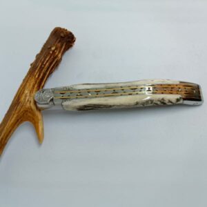Couteau Laguiole "Roi des Forêts" fermé, posé à côté de sa poignée en bois de cerf. Le design sophistiqué révèle les platines en laiton et inox guillochées sous le manche en bois de cerf, reflétant le luxe et la qualité de Laguiole Laffont.