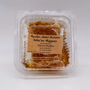 Miel en Rayon du Rucher Saint-Antoine présenté dans une boîte transparente, avec une étiquette artisanale. Miel brut encapsulé dans de la cire naturelle, récolté en Corrèze.